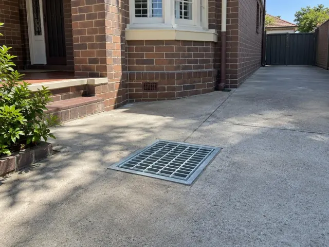 Driveway grate beside a brick house and concrete paving in Five Dock