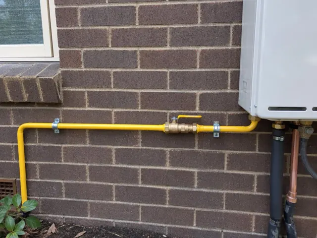 Yellow gas pipe and shutoff valve on a brick exterior wall beside an appliance in Croydon