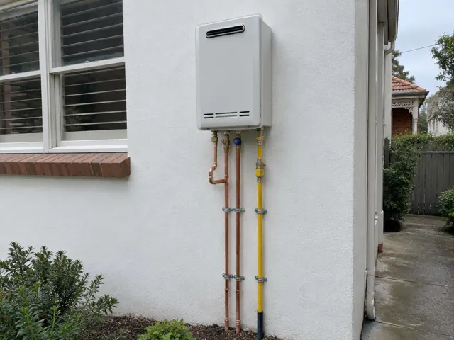 Wall-mounted outdoor hot water unit with exposed pipes beside a house wall in Haberfield