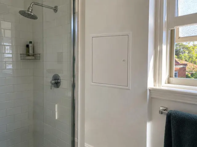 Bathroom shower wall with a small access panel beside a window in Haberfield